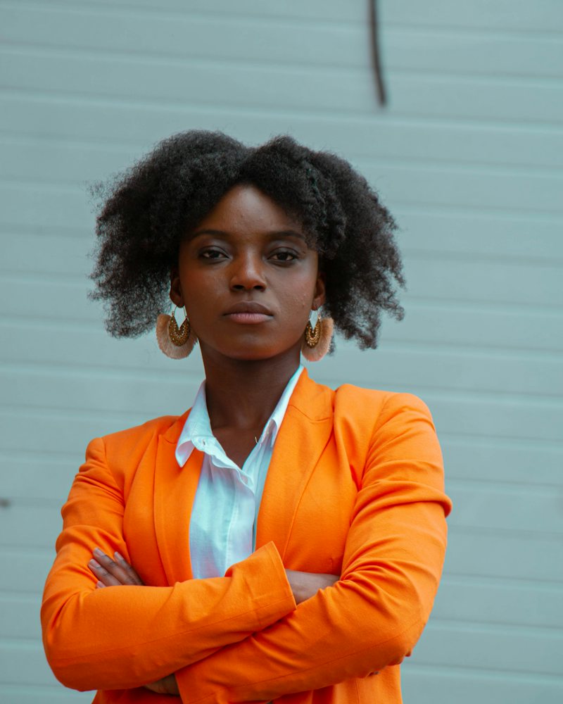 Une cheffe d'entreprise ouest-africaine, bras croisés, en veste orange.